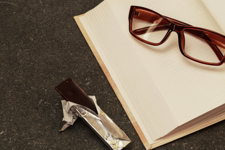 Reading glasses on an open book and chocolates on a granite coffee table.の写真素材