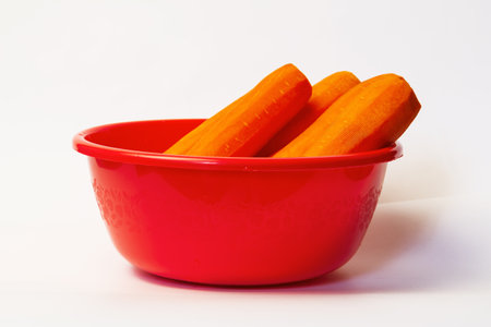 Fresh peeled several stacked carrots in red bowl isolated on white backgroundの写真素材