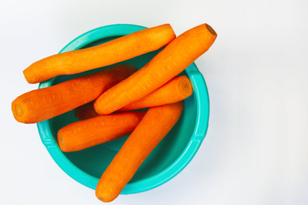 delicious fresh peeled carrots in blue bowl with top view on white backgroundの写真素材