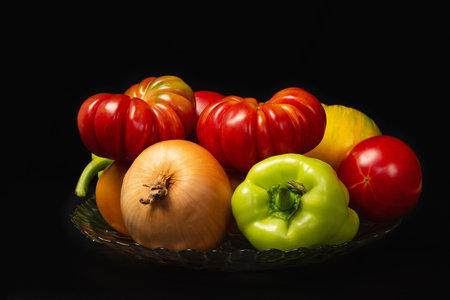 Fresh red and yellow tomatoes with sweet peppers and onions on a glass plate with a black backgroundの写真素材
