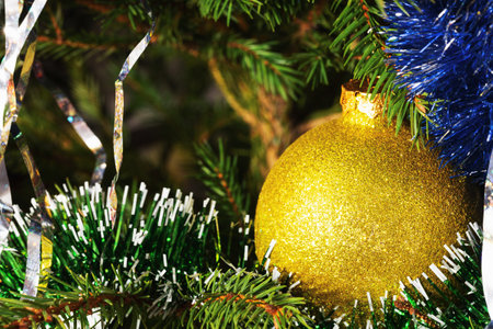 Yellow festive ball with sparkles among the rain and sweets on a branch of a festive Christmas treeの写真素材