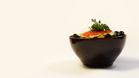A salad with sliced salmon, white feta cheese, fresh tomatoes, cucumbers, arugula, basil, and parsley on a plate. Served in a clay bowl, this healthy vegetarian salad is garnished with red caviar and olives. Front view.の写真素材