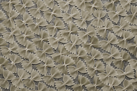 A creative pattern with bronze-colored spaghetti farfalle, food background. Raw pasta, a chef's...