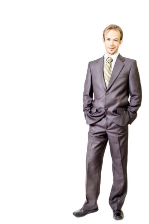Young businessman smirks and keeps hands in pockets on white backgroundの写真素材