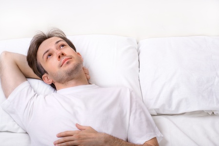 Thinking young man lying on bed and looking awayの写真素材