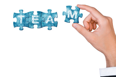 Concept of team - hand connects puzzle piece to build word teamの写真素材