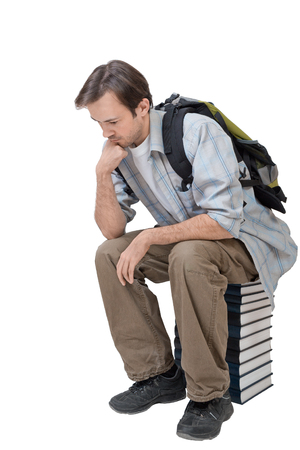 Male student with backpack sitting on the stack of books and thinks - isolated on whiteの写真素材
