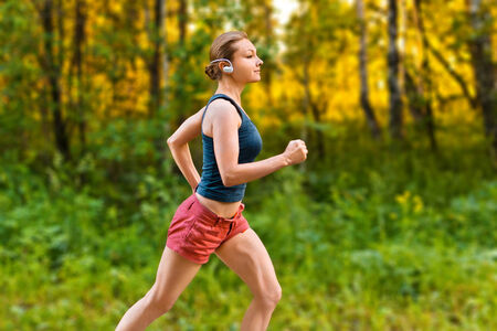 Young sport woman runs on the road through the forestの写真素材