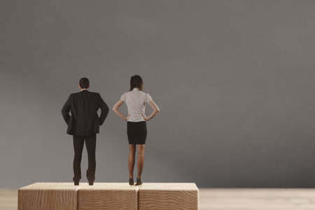 Miniature man and woman standing on the wooden blocks. The concept of the equal opportunities for genders.の写真素材