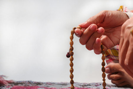 Hands holding prayer beads on a white background. Muslim man sitting on a prayer mat while praying.の写真素材