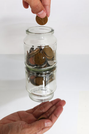 A hand offering a coin to a jar, symbolizing generosity and financial contribution.の写真素材