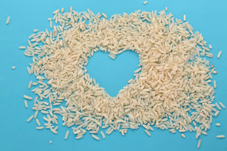 White raw rice in the shape of a heart on a blue background. Top view.の写真素材