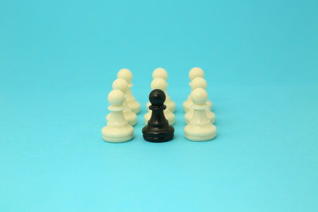 A close-up view of a black pawn, surrounded by white pawns on a blue background.の写真素材
