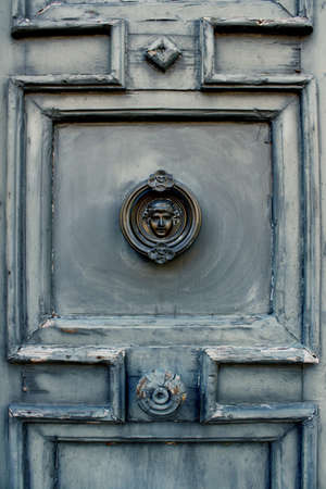 An antique blue gray doorway with bronze decorative face