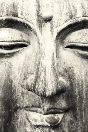 A close up of a beautiful sculpture carved in stone face of Buddha in black and white with a little sepia filterの写真素材