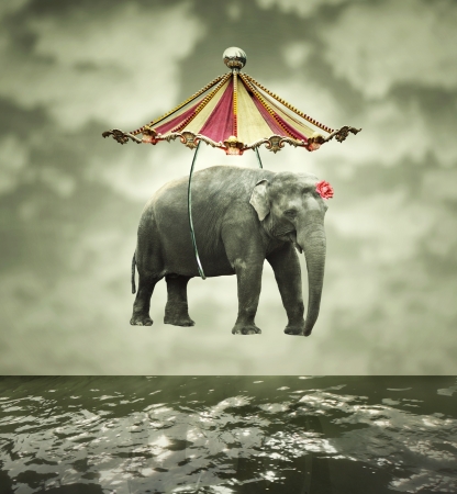 Fanciful and artistic image that represent a flying elephant with circus tent above the waterの写真素材