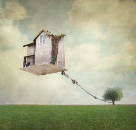 Artistic image representing an house floating in the air tied to a rope to the tree in a surreal vintage backgroundの写真素材