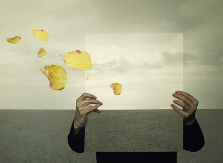 Surreal landscape with a person who holds a framework with the same landscape in the background like an optical effect and leaves in the windの写真素材