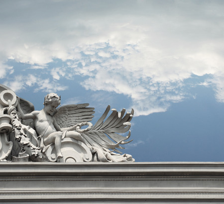 Beautiful little angel on the top of the edge of a building with a sky and clouds in the backgroundの写真素材