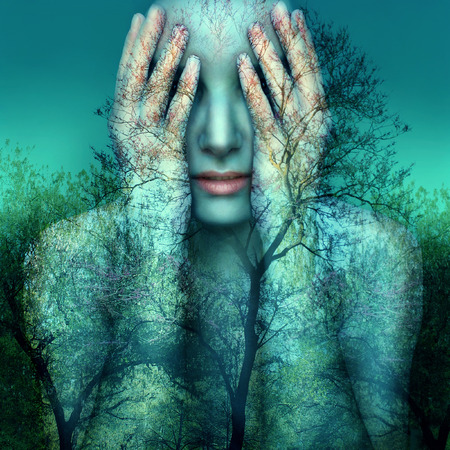 Surreal and artistic image of a girl who covers her eyes with her hands on a background of trees and skyの写真素材
