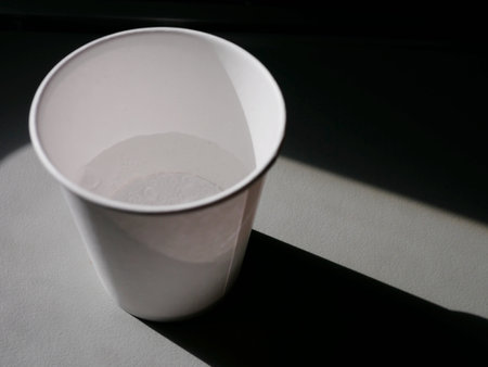 White paper cup on a black and grey background with shadow from the window.