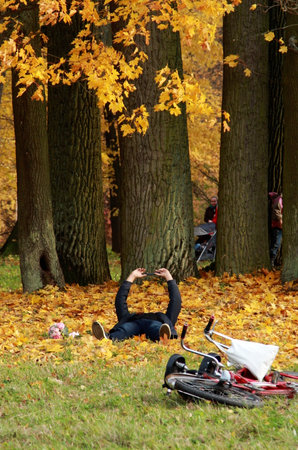 Man lying on the ground in the autumn park with his bikeの写真素材