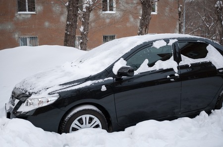 Black car covered with snow standing in snow near the house. Winter picture.の写真素材
