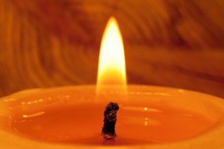 Close-up of wick and flame of burning candle on wood annual rings background.