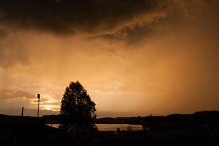 Stormy sky and silhouettes of village at sunset in summer.の写真素材