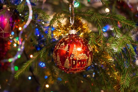 Colorful Christmas background. Christmas toy red glass ball, painted with gold, hangs on the fir tree.の写真素材