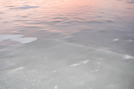 Icy surface of river with crack illuminated by morning winter sun.の写真素材