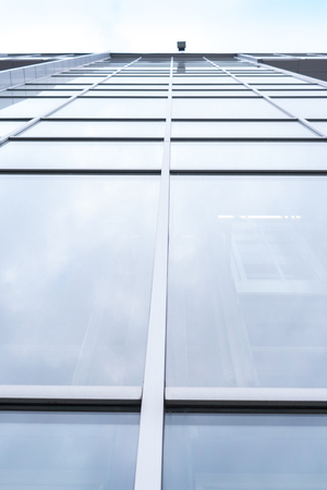 Shooting from lower angle close-up large glass windows of multi-storey office building.