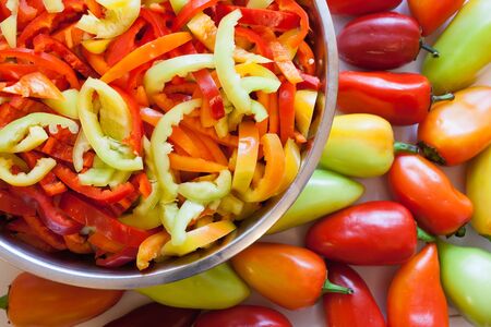 Part of round metal bowl wiht pieces of multi-colored peppers and whole uncut peppers.の写真素材