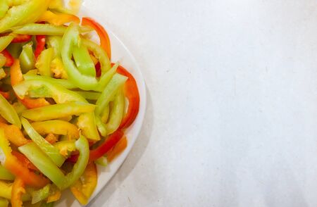 Part of white plate with sliced lengthwise stripes of ripe multi-colored peppers on old white scratched table.の写真素材