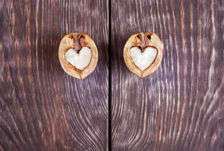 Two halves of walnut in shape of heart are lying on two part of dark painted wooden table with textured stripes and copy space. Top view.の写真素材