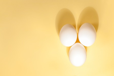 Three white eggs are lying next to each other on a yellow background. Flat lay.の写真素材