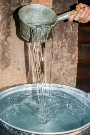 Hand pour water from bucket into the metal pot in rural bathhouse.の写真素材