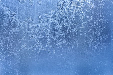 Blue frozen winter glass pane with bizarre frosty pattern of ice crystals.の写真素材