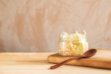 Glass jar with sauerkraut and wooden spoon on wooden cooking board on light background with copy space.の写真素材