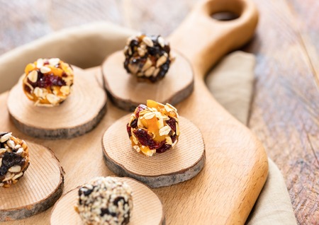 Different kinds of handmade energy balls are lying on wooden saw cuts on kitchen cutting board on...