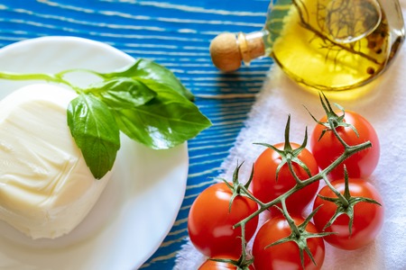 Red tomatoes, mozzarella cheese, olive oil and Basil on white kitchen napkin on blue wooden table.の写真素材
