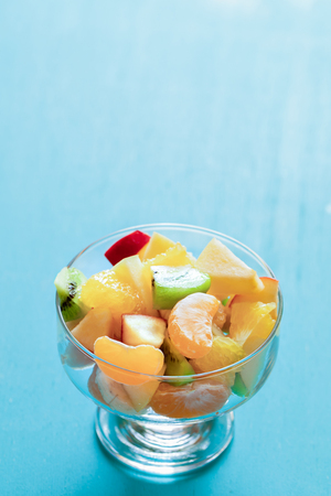 Fresh fruit salad in glass bowl on turquoise background with copy space.の写真素材
