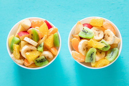 Two white bowls of healthy fresh fruit salad on turquoise background.の写真素材