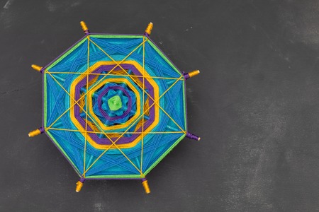 Multicolored handmade mandala on dark grey background.