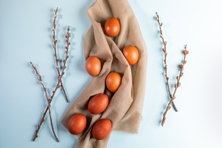 Easter eggs on beige textile with willow branches on pale blue background. Easter card.の写真素材
