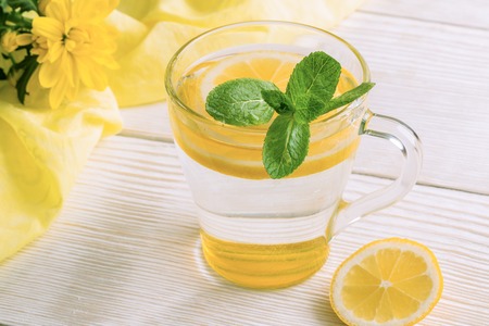 Close-up glass of water with lemon and mint on wooden table with yellow cloth.の写真素材