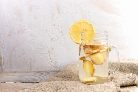 Glass jar with ginger water on burlap on wooden table on light  background.の写真素材