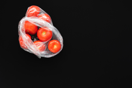 Red ripe tomatoes in open plastic bag on black background.の写真素材