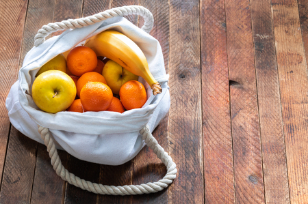 Close-up ecologic white linen bag of fruits on old wooden table.の写真素材