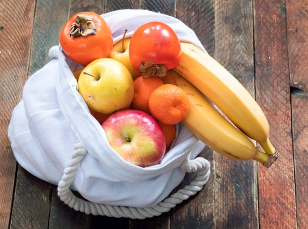 Close-up white linen bag of fruits is standing on wooden table.の写真素材